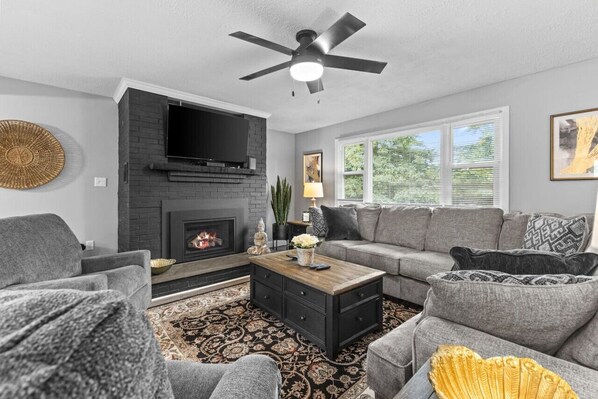 A living room with a fireplace, grey sofas, a coffee table, and a ceiling fan.