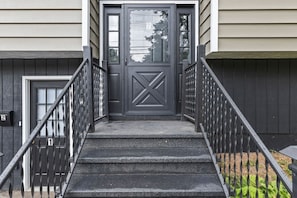 A set of exterior stairs leading to a dark-colored door with a geometric design, flanked by metal railings. - Cute 3BR APT - So Burlington (South Burlington)