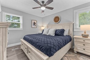 A bedroom with a bed, a ceiling fan, a nightstand, a lamp, and a wall decoration.