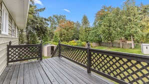 A wooden deck with a lattice railing, surrounded by a grassy yard and trees. - Cute 3BR APT - So Burlington (South Burlington)