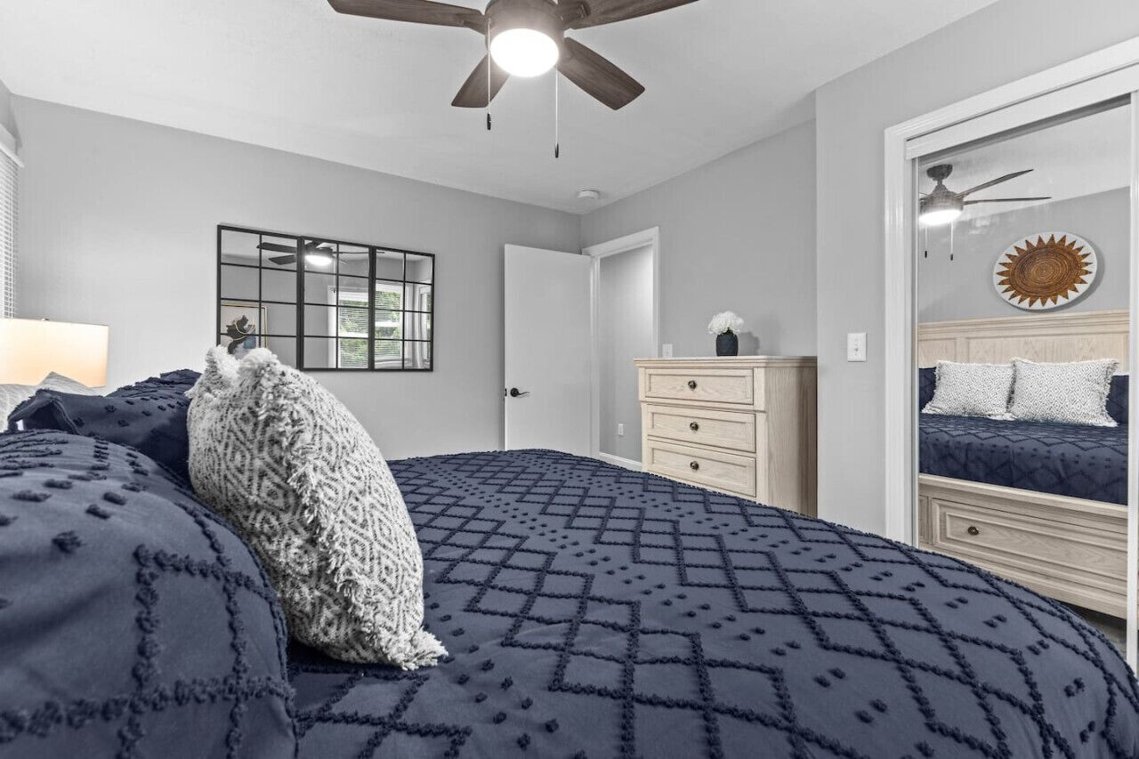 A bedroom with a bed, a dresser, a mirror, and a ceiling fan.