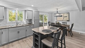 A modern kitchen with grey cabinets, a large island, and a dining area with a table and chairs. - Cute 3BR APT - So Burlington (South Burlington)