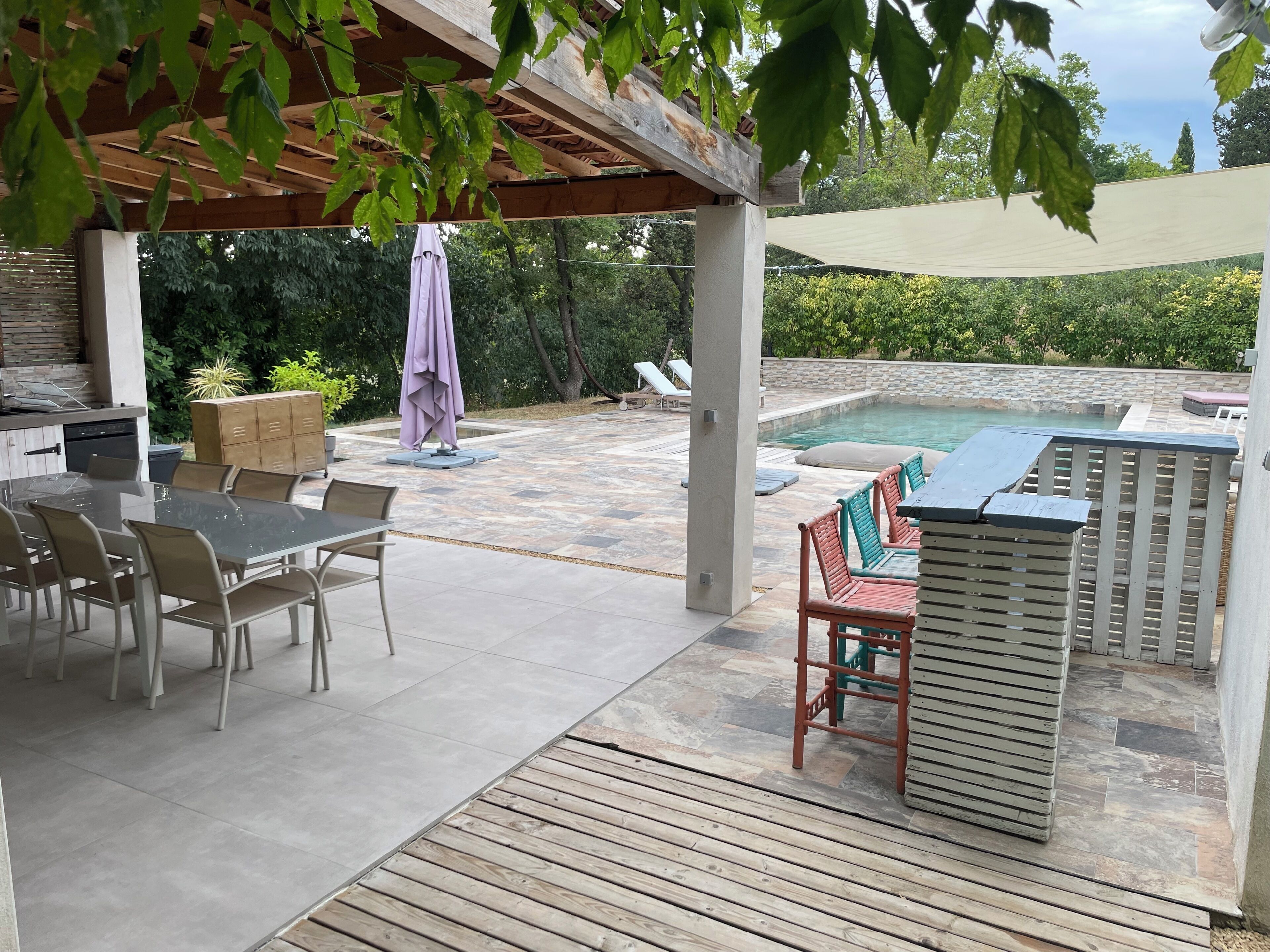 Une terrasse extérieure avec une piscine, un espace repas couvert et un barbecue.
