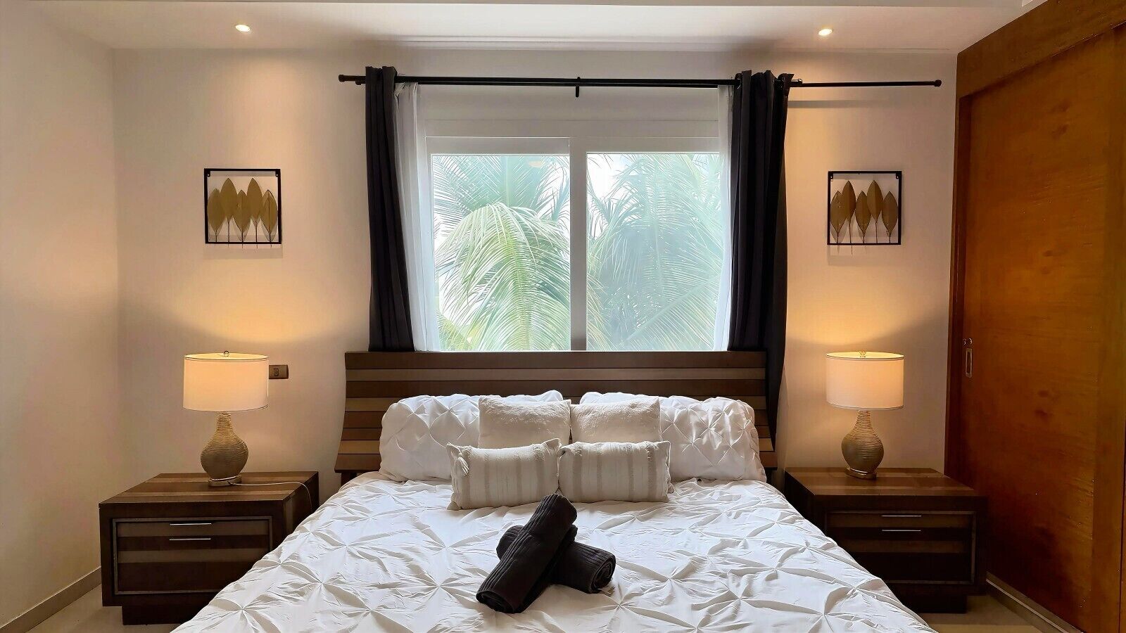 Una camera d'hotel con un letto, due comodini, una finestra con tende e due lampade a parete.