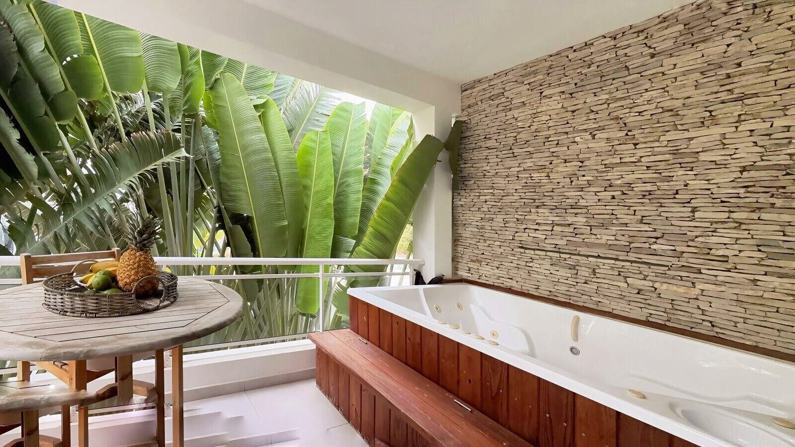 A balcony with a wooden table, a wicker basket with fruits, and a stone wall.