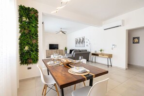 Un comedor moderno con una mesa de madera preparada para una comida, un jardín vertical verde, un sofá gris y una decoración de estilo minimalista.