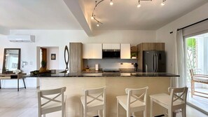 A modern kitchen with white cabinetry, a central island, and a dining area with white chairs.
