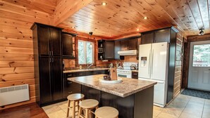A modern kitchen with dark wood cabinets, a granite countertop, a central island with stools, a white refrigerator, and a stove.