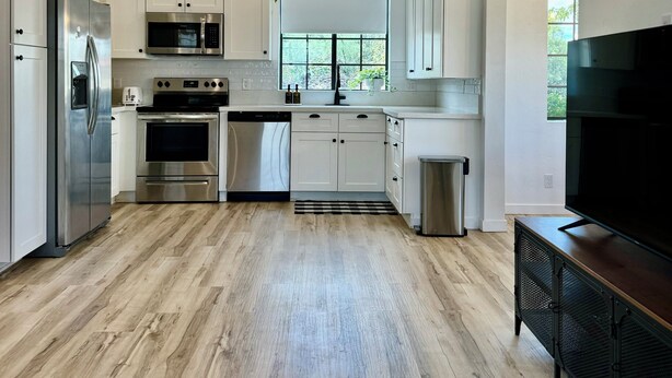 Una cocina moderna con armarios blancos, electrodomésticos de acero inoxidable y un amplio ventanal que proporciona luz natural.