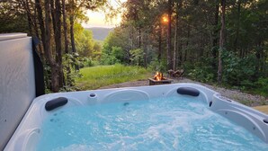 A hot tub in a forested area with a fire pit nearby. - New Farm Cottage, near Branson, MO built in 2022 (Walnut Shade)