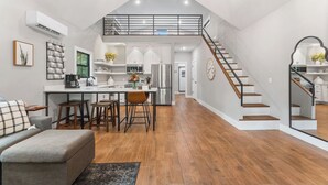 A spacious living area with a kitchen, dining table, and a staircase leading to an upper level. - New Farm Cottage, near Branson, MO built in 2022 (Walnut Shade)