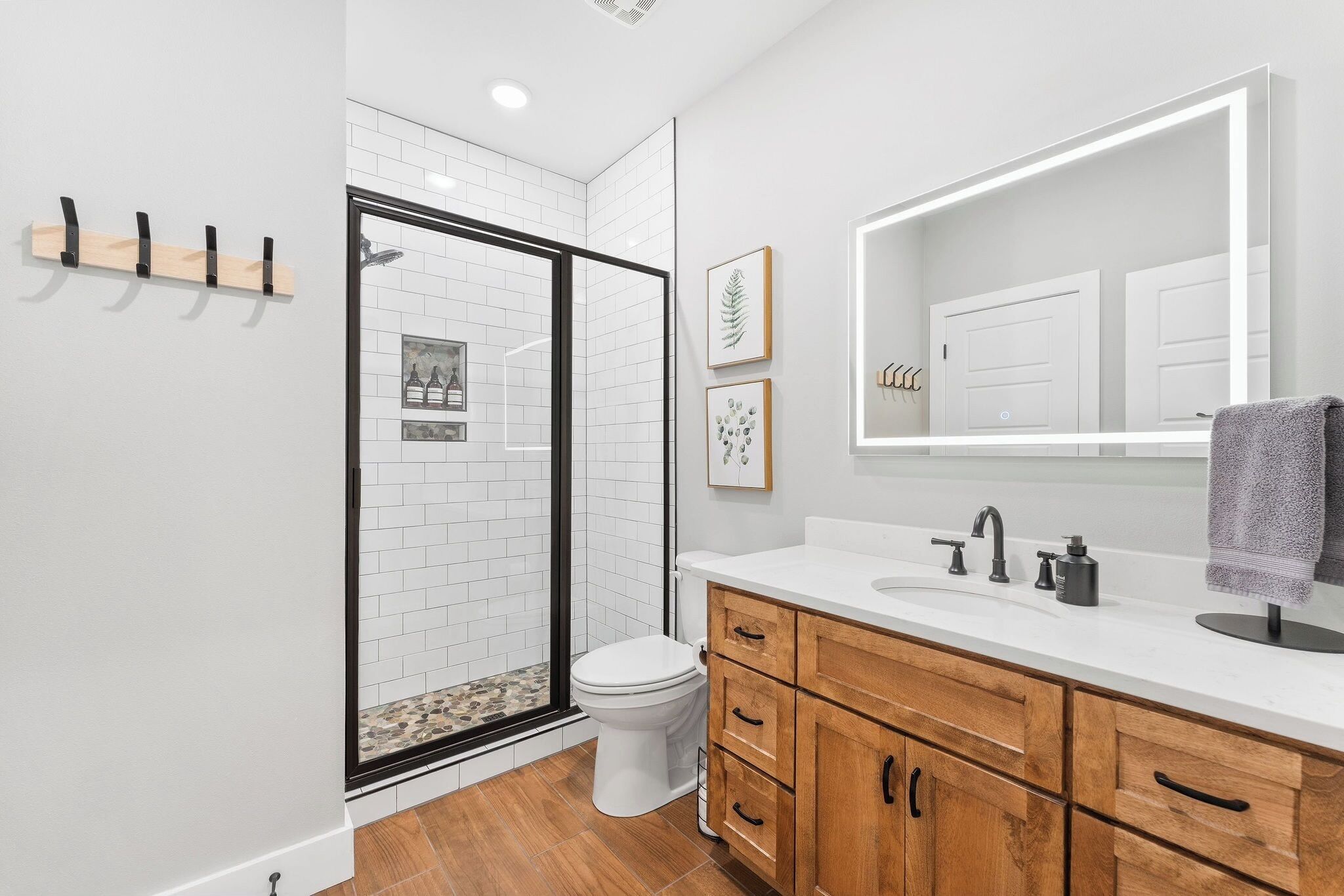 A modern bathroom with a glass shower enclosure, white tiled walls, a wooden vanity with a sink, and a large mirror.