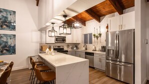 A modern kitchen with a large island, stainless steel appliances, and hanging pendant lights.