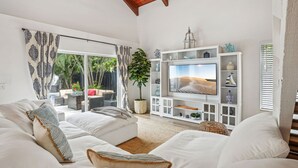 A modern living room with a white sofa set, a large flat-screen TV, and a white entertainment unit with decorative items.
