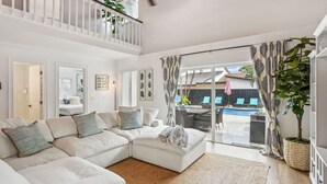 A modern living room with a sectional sofa, a ceiling fan, and a view of an outdoor pool area.
