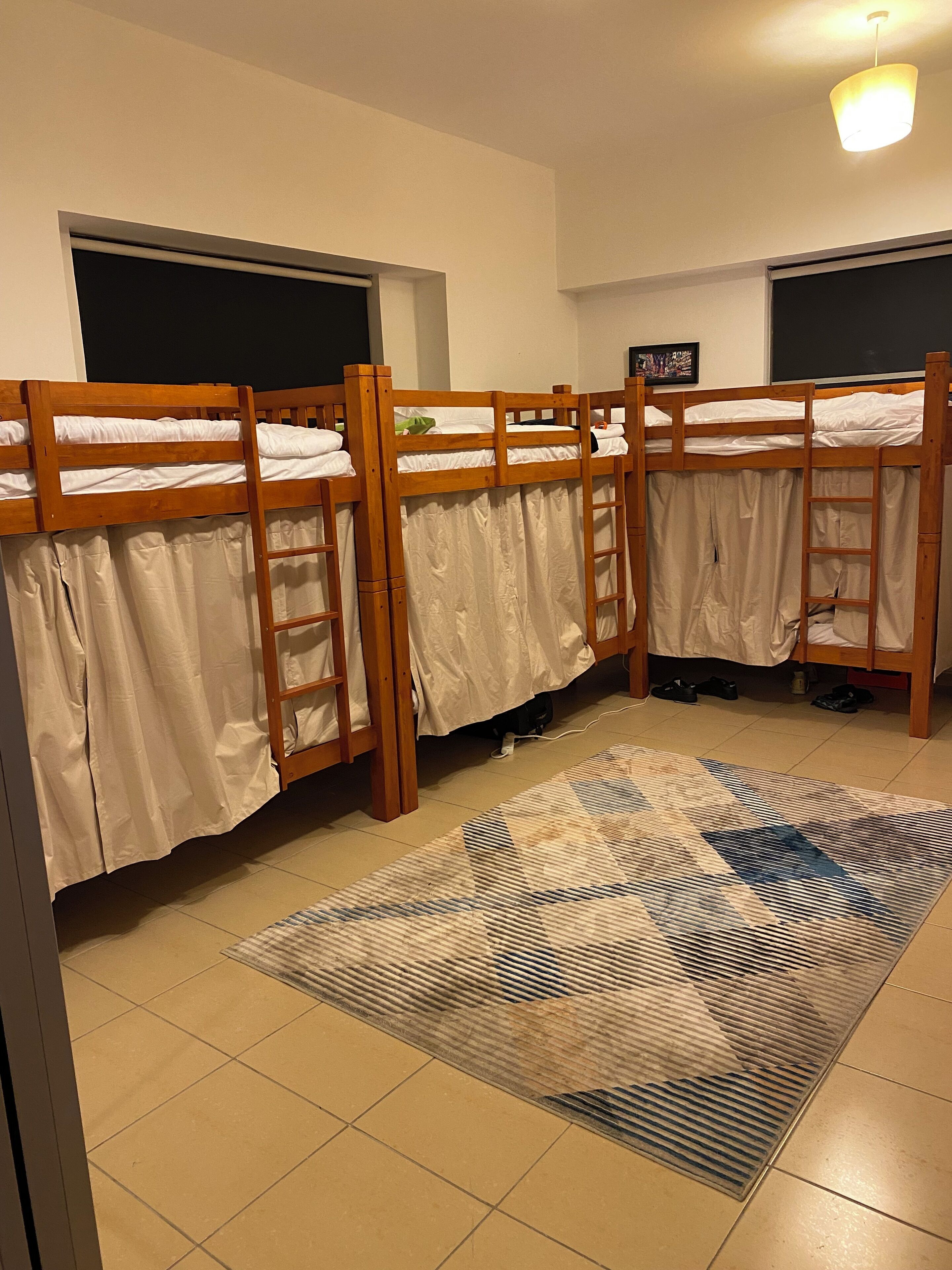 Um quarto em dormitório com beliches, um tapete estampado e uma luminária no teto.