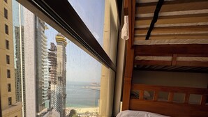 Hotelkamer hoog in een wolkenkrabber met een groot raam, uitzicht op zowel een stadsbeeld als een strand.