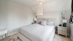 A bedroom with a large bed, a hanging light fixture, two bedside tables, and a nightstand.