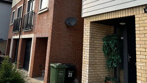 A residential building with a brick facade, a satellite dish, and a potted plant near the entrance.