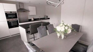 A modern kitchen with built-in appliances, a dining area with a gray table and chairs, and a decorative white flower arrangement.