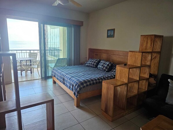 Une chambre à coucher avec un lit, une tête de lit en bois, une petite table et un balcon avec des chaises.