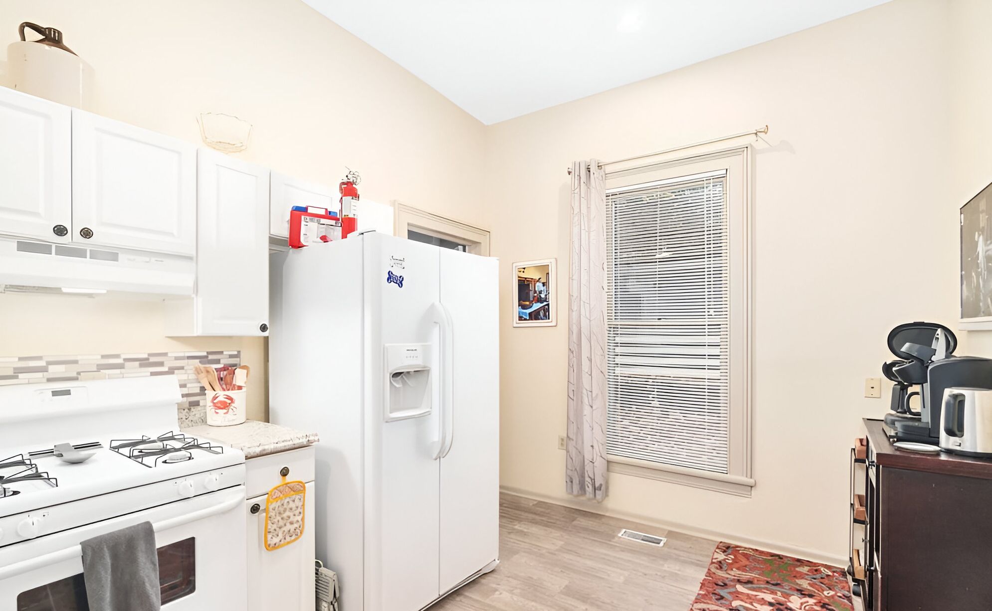A compact kitchen with white cabinets, a refrigerator, a stove, and a window with blinds.