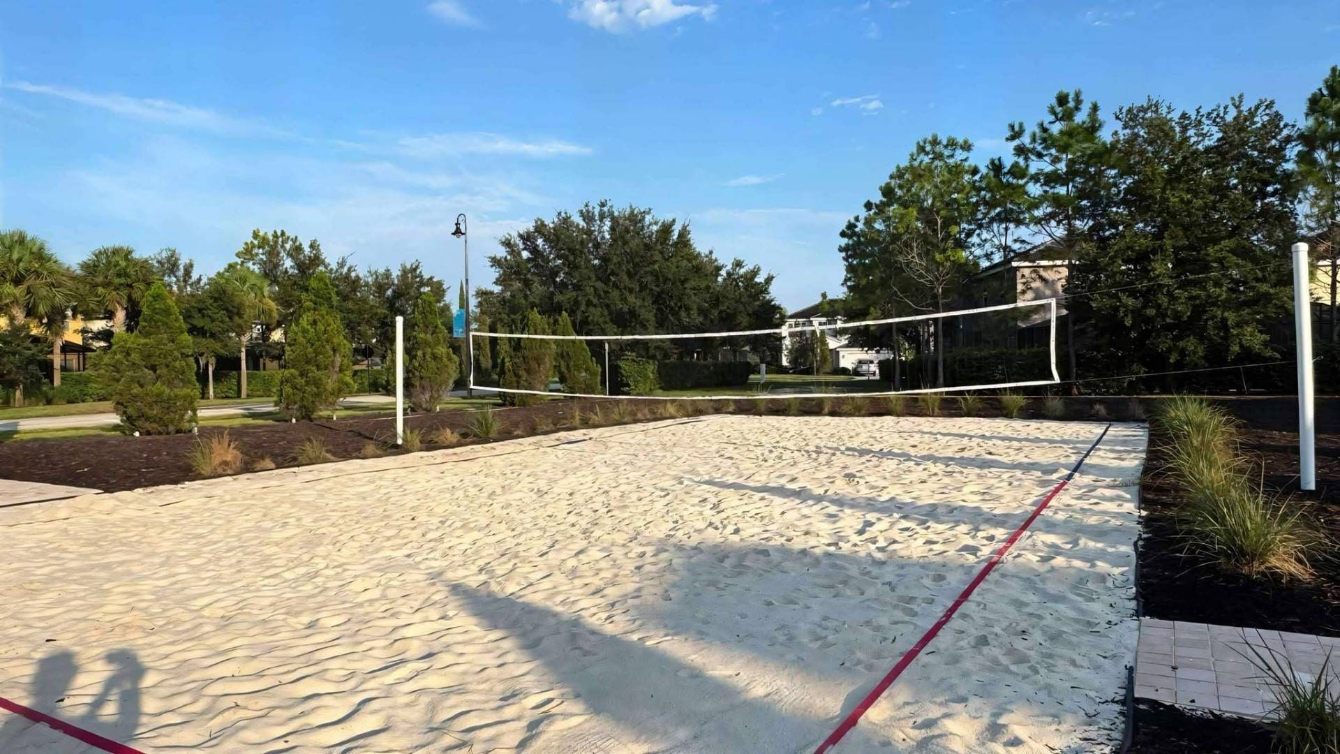 Ein Sandvolleyballfeld mit Netz, umgeben von Bäumen und einem Gebäude im Hintergrund.