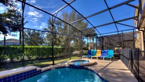 A covered outdoor swimming pool with a hot tub, surrounded by lounge chairs and a view of a residential area.