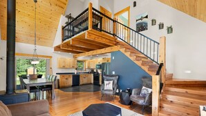 Un vaste espace de vie doté d’un haut plafond, d’un escalier en bois et offrant une vue sur la cuisine.