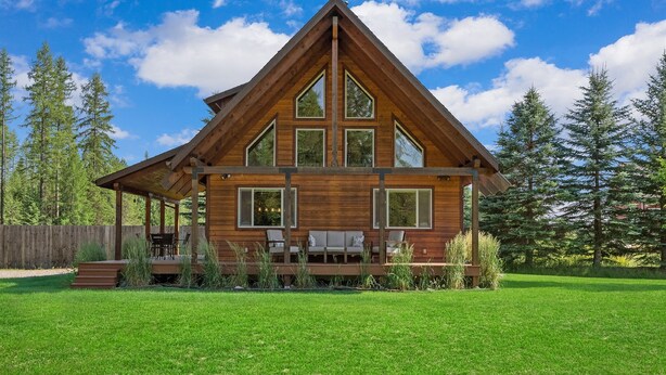 Une cabane en bois avec un toit triangulaire, de grandes fenêtres et une terrasse dotée de meubles d’extérieur.