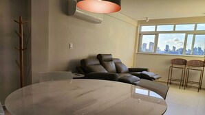 Egy modern nappali, melyben kerek asztal, bőrkanapék találhatók, és nagy ablakokon keresztül nyílik kilátás a városra.