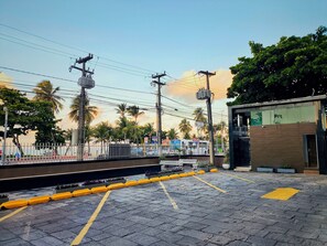 Egy burkolt terület, sárga oszlopokkal, egy busz és egy modern stílusú épület.