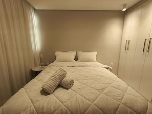 A hotel room with a large bed, a nightstand, and a wardrobe. - Apartamento no Edifício Beira Mar (João Pessoa)