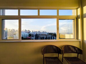 A room with a large window overlooking a cityscape. There are two chairs in the room. - Apartamento no Edifício Beira Mar (João Pessoa)