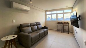 A modern living room with a leather sofa, a small round table, and a TV mounted on the wall.