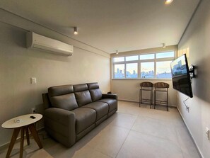 A modern living room with a leather sofa, a small round table, and a TV mounted on the wall. - Apartamento no Edifício Beira Mar (João Pessoa)
