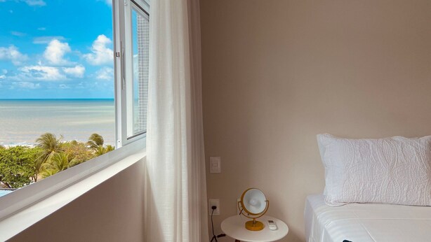 Ett hotellrum med en säng, ett litet bord med en spegel och utsikt över havet.