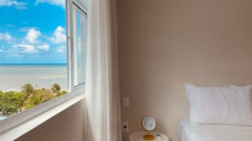 Quarto de hotel com cama, uma mesinha com espelho e vista para o oceano.