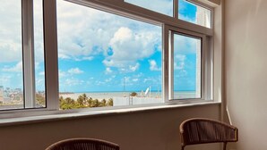 A room with a large window overlooking a beach, two wicker chairs, and a white wall.