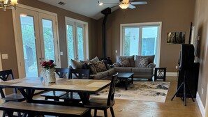A spacious living room with a large sofa, a dining table with benches, and a ceiling fan. - Beulah Land Only 4 Miles from SNP! (Three Rivers)
