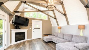 A room with a fireplace, a sectional sofa, a television mounted on the wall, and a ceiling with exposed wooden beams.