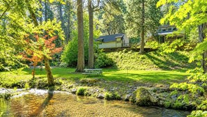 A serene lakeside setting with a house, a picnic table, and a small bridge.