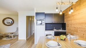 A modern kitchen with a wooden wall, a dining table set with plates and cutlery, and a fruit bowl.