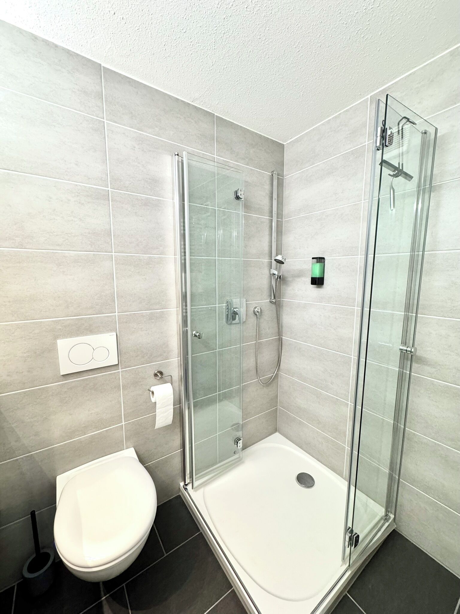 A modern bathroom with a glass-enclosed shower, a white toilet, and a visible hand dryer.