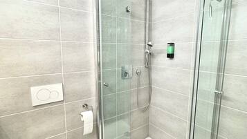 A modern bathroom with a glass-enclosed shower, a white toilet, and a visible hand dryer.
