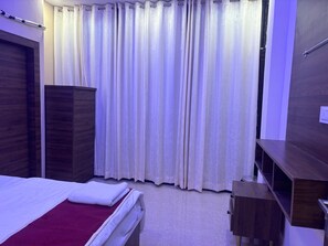 A bedroom with a bed, a wooden wardrobe, a desk, and a curtain. - Radhe Krishna Radiant (Mathura)