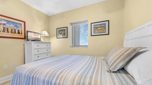A bedroom with a bed, a dresser, a window, and wall art.