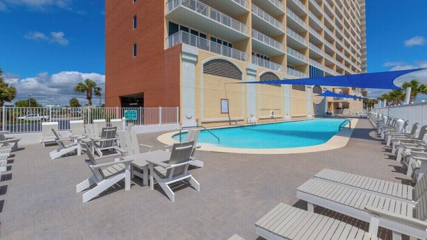 A hotel with a swimming pool, lounge chairs, and a building with balconies.