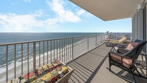 A balcony with a view of the beach and ocean, wicker furniture, and a wooden table with a colorful tablecloth.