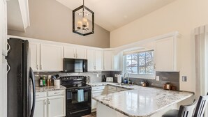 A kitchen with white cabinets, a black refrigerator, a granite countertop, a black stove, and a hanging light fixture. - Spacious Home Near Tennyson & Olde Towne - Sauna + Massage Chair + WiFi (Arvada)